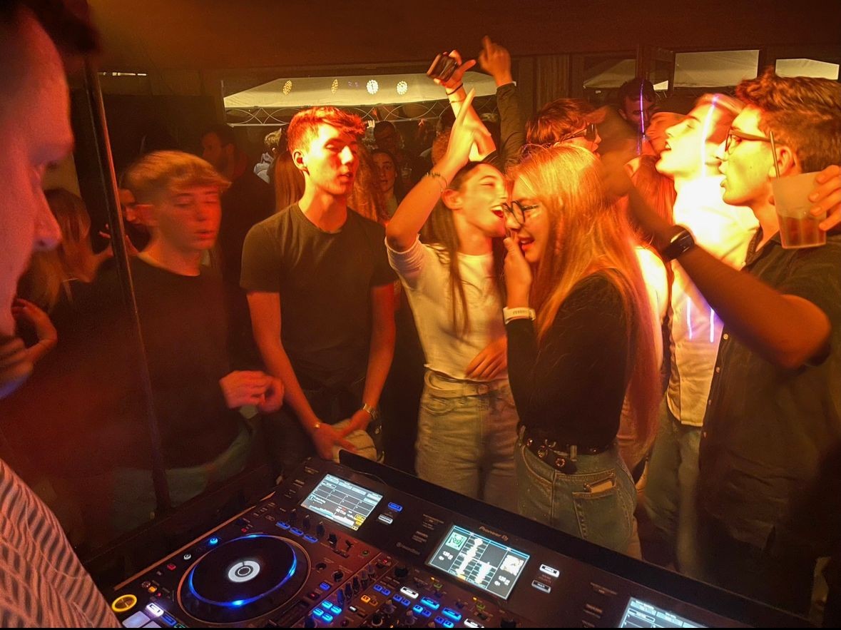 Group of young people dancing near a DJ booth at a lively party.