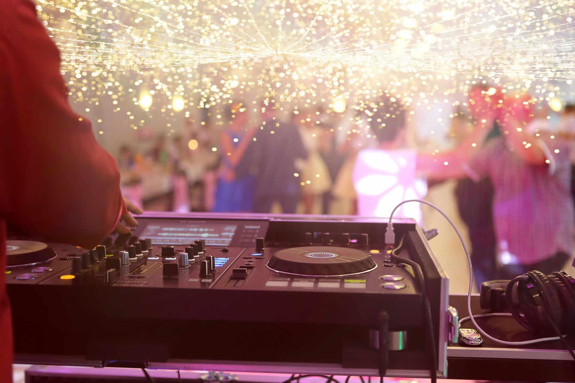 Mixing console is played by DJ and couples dancing on the dance floor in the background